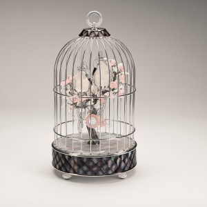"Cage à oiseaux" - CHANEL Joaillerie Dans le salon de l'appartement de Gabrielle Chanel rue Cambon, posée sur une table basse, une précieuse cage abrite deux inséparables oiseaux en nacre. Librement inspirée par cette cage miniature, la "Cage à oiseaux", pièce unique d'exception, réunit les savoir-faire de la Haute Joaillerie et de l'Horlogerie : sculpture, marqueterie de nacre et sertissage, autant de métiers d'art qui mettent en valeur cette pièce de collection. Ce gracieux tête-à-tête se joue au cur d'un décor où fleurs de camélia, plumes, matelassé, contraste du noir et du blanc, font écho aux codes stylistiques chers à la Maison. Pendule "Cage à oiseaux" en or blanc 18 carats serti de diamants, tsavorites, pierres de lune, quartz rose, cristal de roche, nacre blanche et noire.