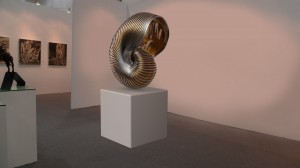 Née en 1983, Fan Xiaoyan est une jeune artiste chinoise qui vit et travaille à Beijing. Elle s’est fait connaître pour ses sculptures de femmes–machines, sortes d’hybrides ou cyborgs, par lesquelles elle évoquait « l’avènement d’une nouvelle ère, d’un nouveau genre humain, d’un nouveau pouvoir, d’un monde virtuel et surréaliste ». Avec sa nouvelle série, elle continue son exploration de l’influence de la technologie sur l’évolution de la Nature et de ses produits, du monde actuel qui devient kafkaïen. Les trois oeuvres présentées ici, un coquillage, produit de la mer et deux produits de la terre sont surdimensionnés, le premier se protégeant, et les deux autres à l’inverse, essayant de se libérer, probablement de cette technologie transformant la nature. Fan Xiaoyan associe la chair, douce et chaude des fruits avec l’acier, solide et froid, et joue avec les contrastes pour nous atteindre tant au niveau visuel que psychologique.