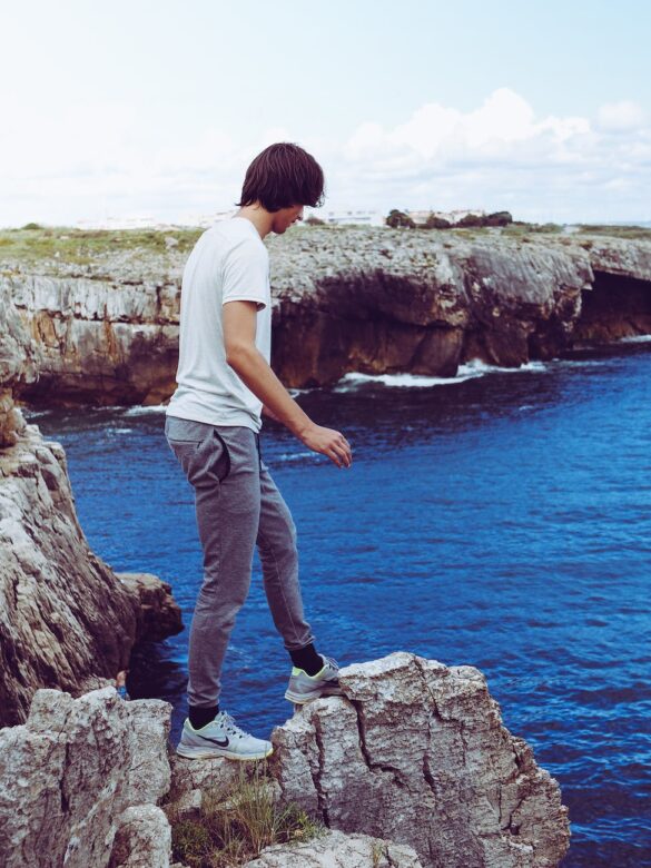 man in white shirt and grey pants standing on cliff