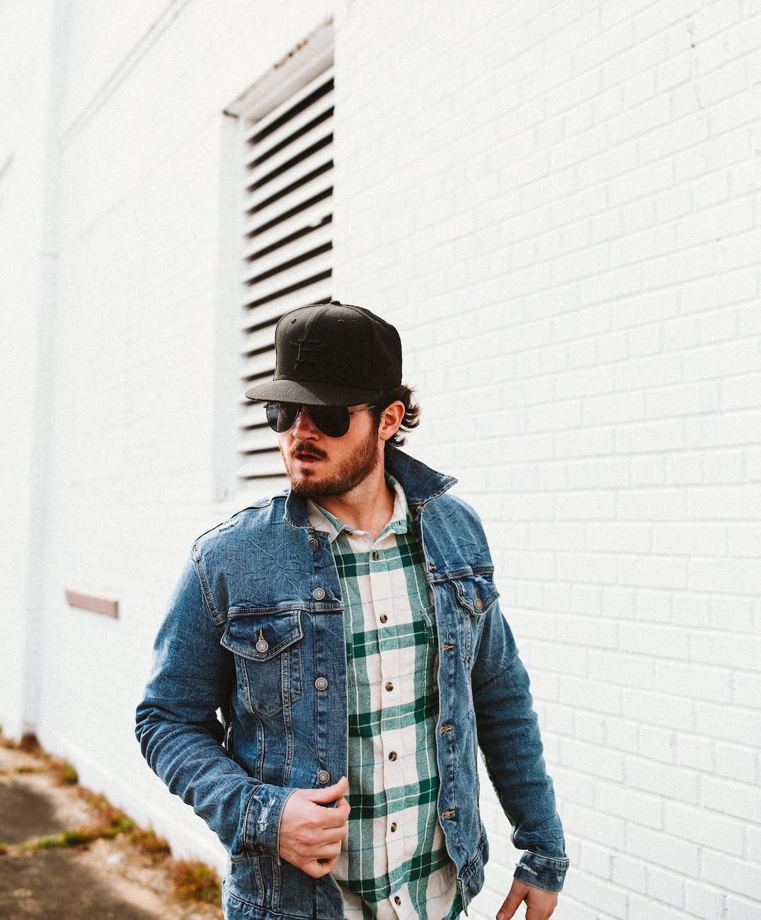 young man in sunglasses in denim jacket and black new era hat